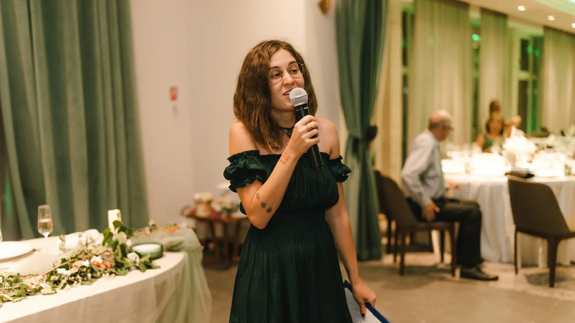 Meda Andreea Căpîlna moderând cu microfonul în mână, într-o sală de evenimente